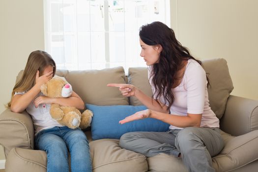 Woman pointing at scared daughter on sofa