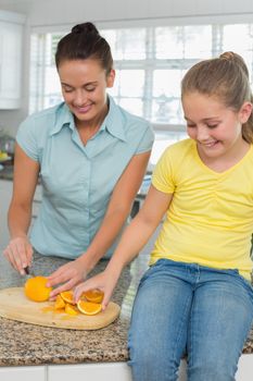 Woman slicing oranges for daughter in kitchen