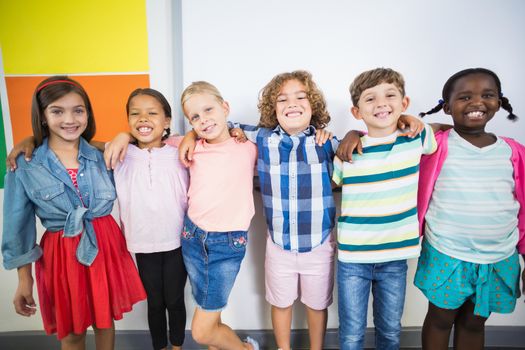 Smiling kids standing with arm around in classroom
