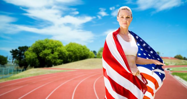 Portrait of sporty woman holding American flag against athletics field on a sunny day 