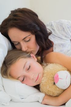 Mother kissing sleeping daughter in bed