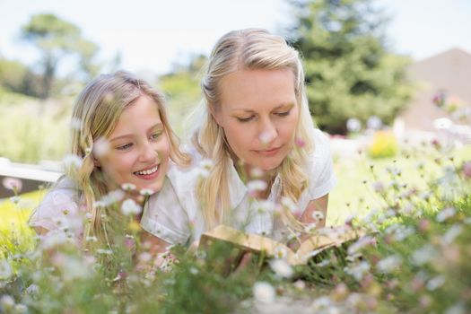 Mother and daughter reading book while lying in park
