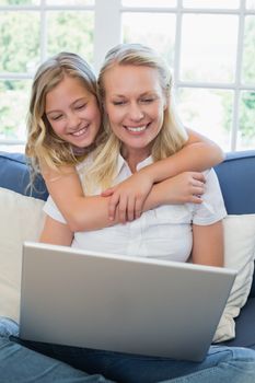 Girl embracing mother using laptop