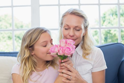 Mother and daughter smelling roses on sofa