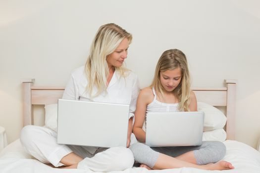 Mother and daughter using laptops in bed