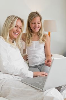 Cheerful mother and daughter using laptop in bed