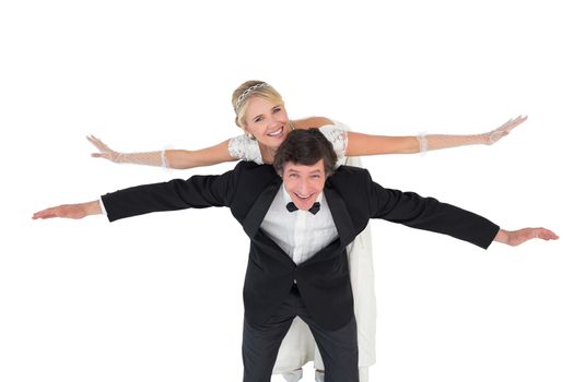 Groom with arms outstretched carrying bride on back