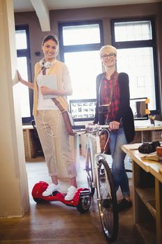 Graphic designer holding bicycle while colleague standing on hover board
