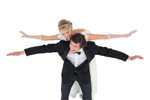 Happy groom with arms outstretched carrying bride on back
