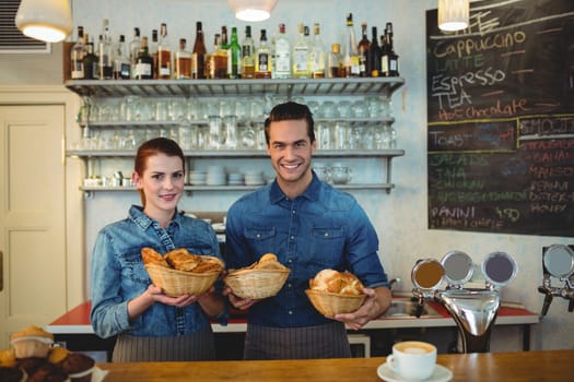 Portrait of happy co-workers with breads at cafe