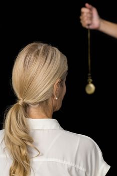 Cropped hand of hypnotherapist holding pendulum by woman