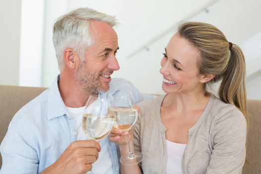 Happy couple sitting on couch toasting with white wine