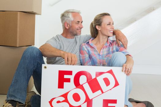 Happy couple sitting on floor with sold sign