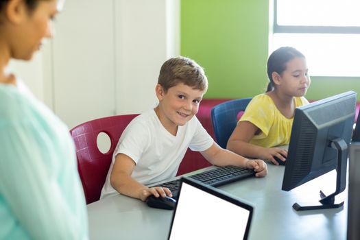 Boy with classmate and teacher using computers