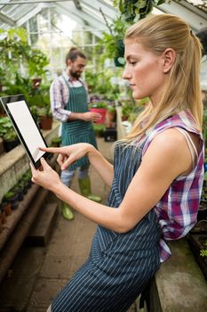 Side view of female gardener using digital tablet at greenhouse