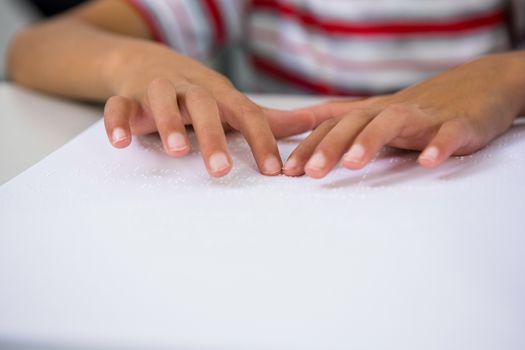 Child reading braille book in classroom