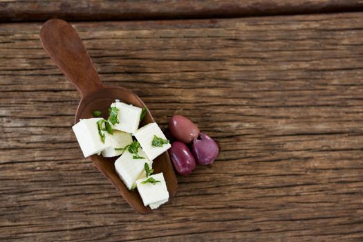 Cheese cubes garnished with herbs and olives on wooden spoon