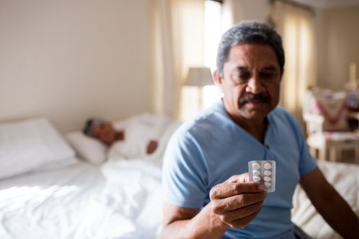 Sick senior man looking at medicine packet in bedroom