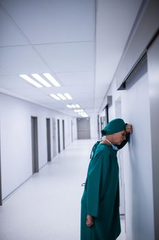 Tensed female surgeon leaning on wall in corridor