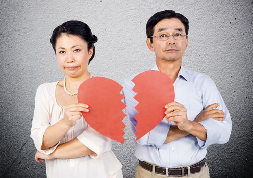 Displeased mature couple holding a broken heart