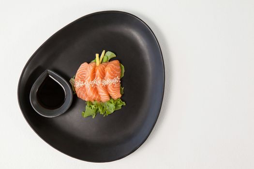Four sashimi sushi served with soy sauce in black plate