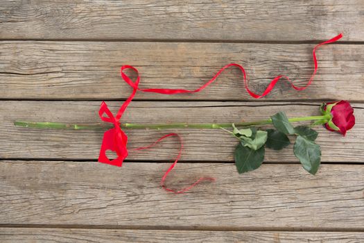 Red rose with ribbons on wooden surface