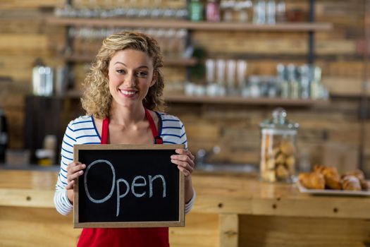 Smiling waitress standing with open signboard in cafe