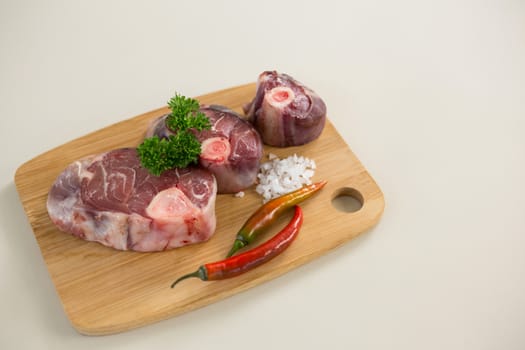 Sirloin chops, salt and chillies on wooden board against white background