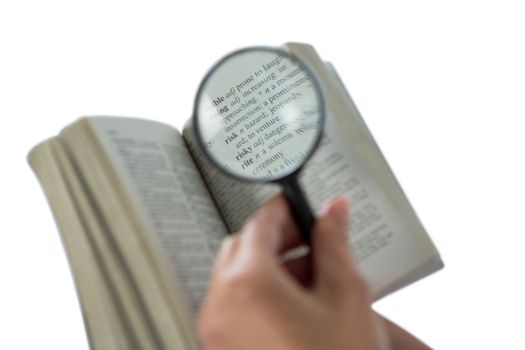 Businesswoman reading a dictionary through magnifying glass
