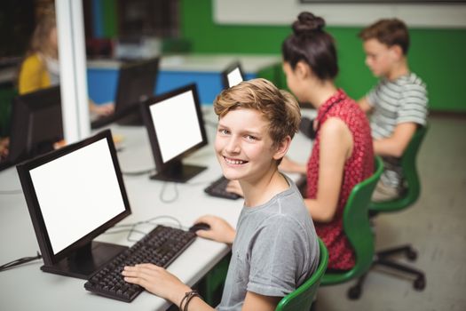 Portrait of smiling schoolboy studying in computer classroom