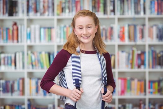 Portrait of schoolgirl standing with schoolbag in library