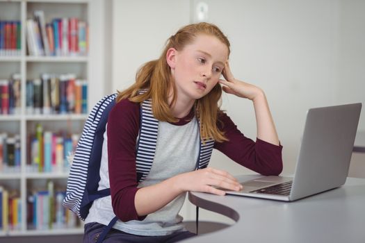 Thoughtful schoolgirl using laptop in library