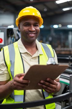 Portrait of smiling factory worker holding clipboard in factory