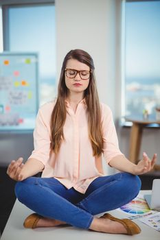 Female graphic designer sitting on table and meditating in office