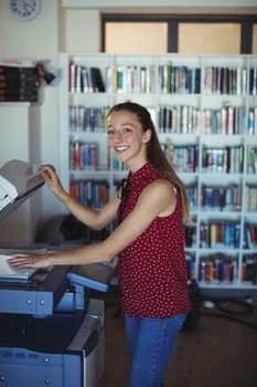 Portrait of happy schoolgirl using Xerox photocopier in library