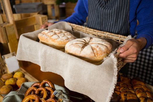 Mid section of staff holding wicker basket of breads at counter
