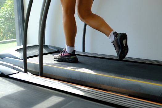 Fitness girl running on track treadmil. Health and sport concept background. Woman with muscular legs in gym workout at fitness gym.