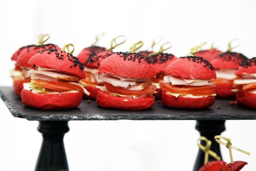 Mini burgers with red bun, stuffed with ham and tomato, sprinkled with black sesame seeds