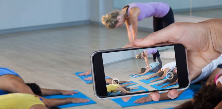 Hand holding mobile phone against white background against yoga instructor helping student with correct pose