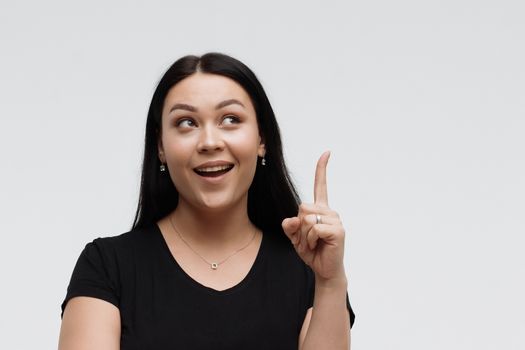 Positive woman in black outfit holding forefinger up