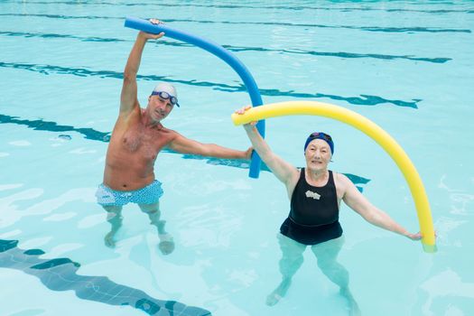 Senior couple exercising with pool noodle in swimming pool