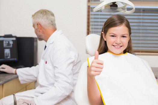 Smiling little girl showing thumbs up in dentists chair