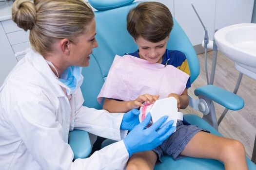 Dentist teaching boy brushing teeth of dentures at medical clinic