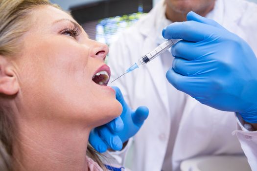 Close up of dentist holding syringe by patient