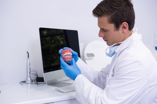 Dentist holding dental mold while sitting by computer