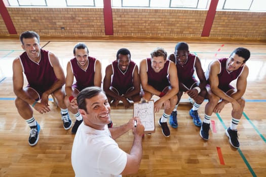 Smiling coach explaining game plan to basketball players