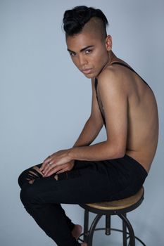 Transgender wearing suspenders sitting on stool over gray background