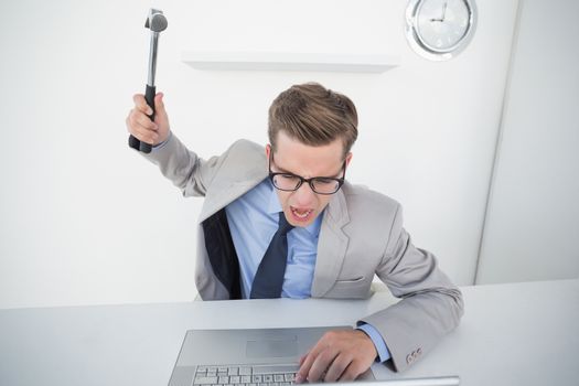 Angry businessman holding hammer over laptop in his office