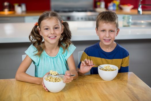 Portrait of smiling sibling having breakfast cereal in kitchen