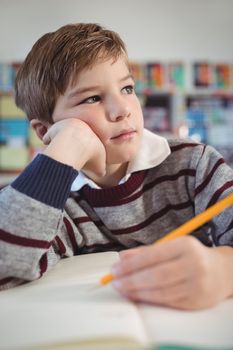 Thoughtful schoolboy studing while sitting at desk